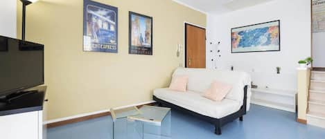 A living room with a sofa, a glass coffee table, a television, and wall art.
