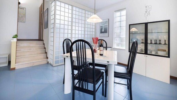 A dining area with a white table, black chairs, a hanging light, and a glass cabinet with dishes.