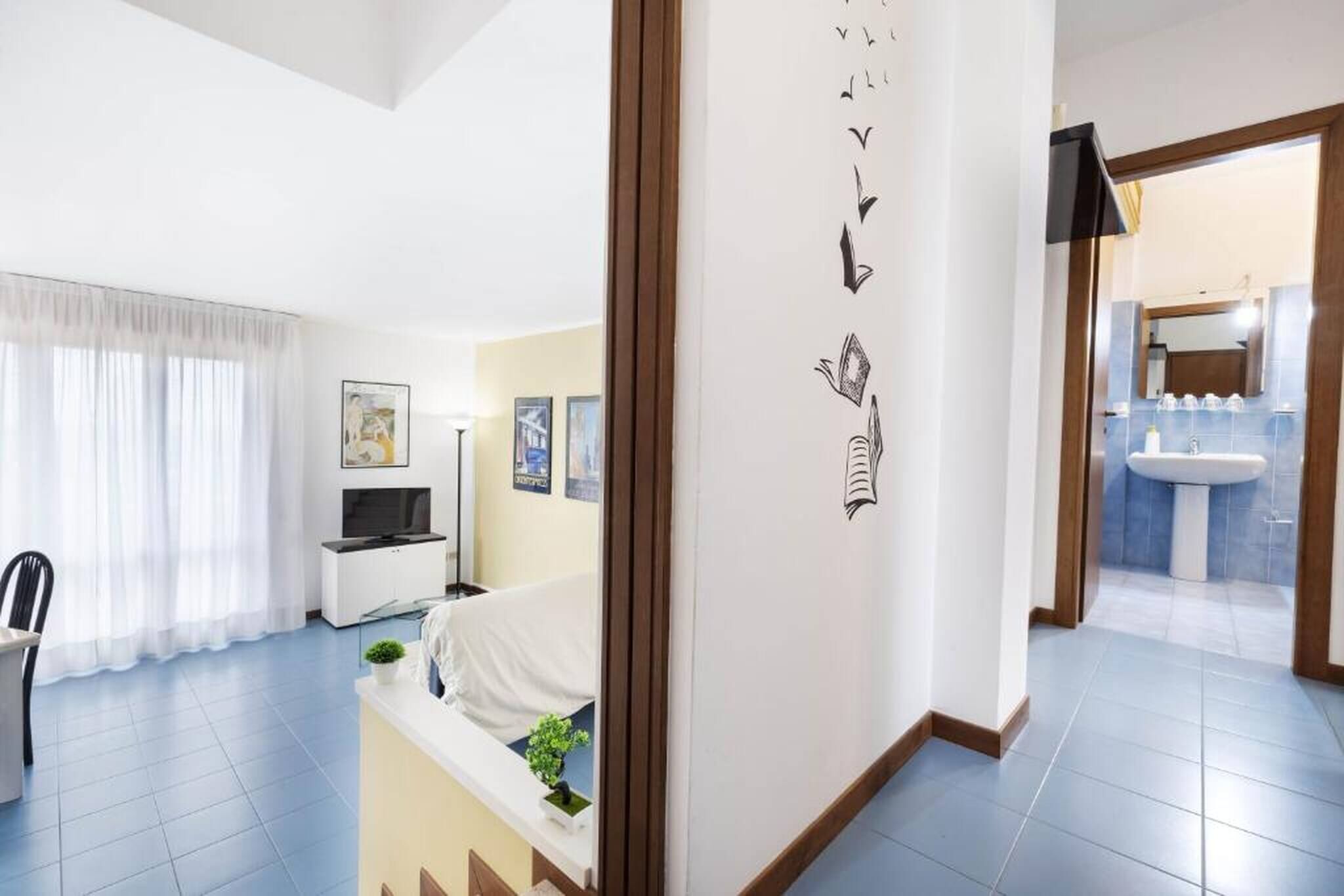 A modern hotel room with a bed, a TV, a desk, and a window with curtains.