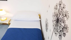 A bed with a blue bedspread, a white pillow, and a wall with a dandelion illustration.