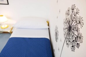 A bed with a blue bedspread, a white pillow, and a wall with a dandelion illustration.