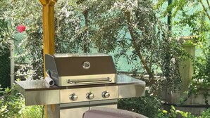 Um pátio externo com toalha de mesa xadrez, cadeiras de vime, churrasqueira e mesa com controle remoto.