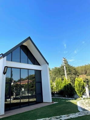 Une maison moderne dotée d’une grande façade vitrée, d’un toit en pente et d’une pelouse bien entretenue.