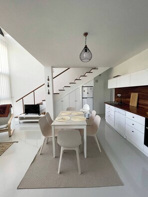 Une cuisine moderne avec des meubles blancs, un coin repas comprenant une table et des chaises, et un escalier menant à un autre niveau.