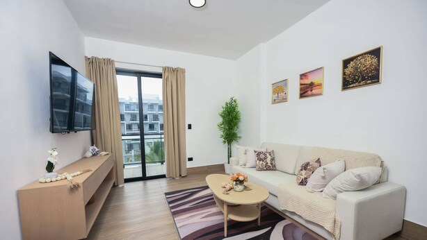 Un salon moderne avec un canapé, une table basse, un téléviseur et un balcon agrémenté de rideaux.