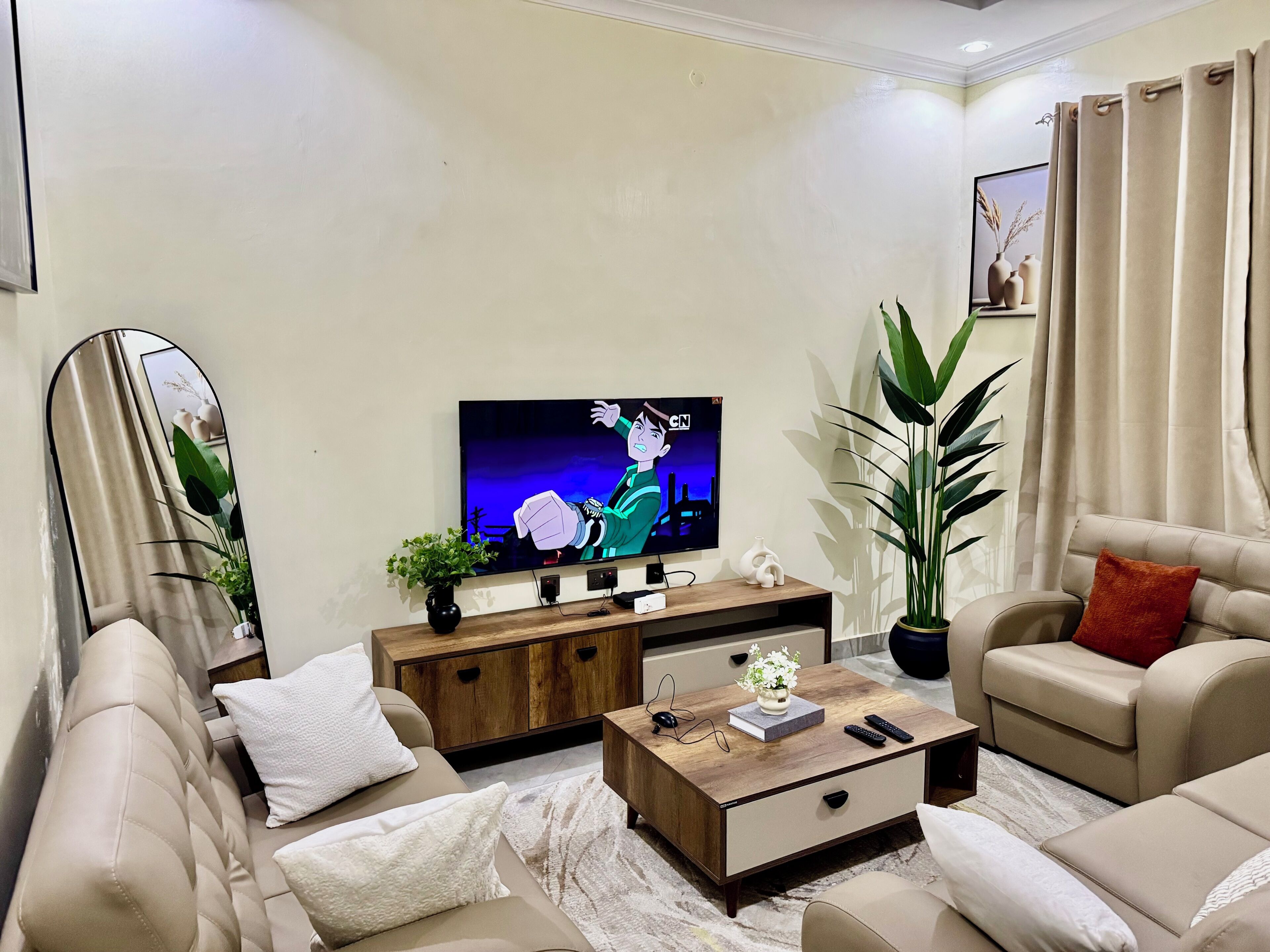 A modern living room with a flat-screen TV, comfortable sofas, a coffee table, and a large plant.