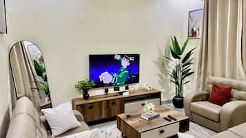 A modern living room with a flat-screen TV, comfortable sofas, a coffee table, and a large plant.