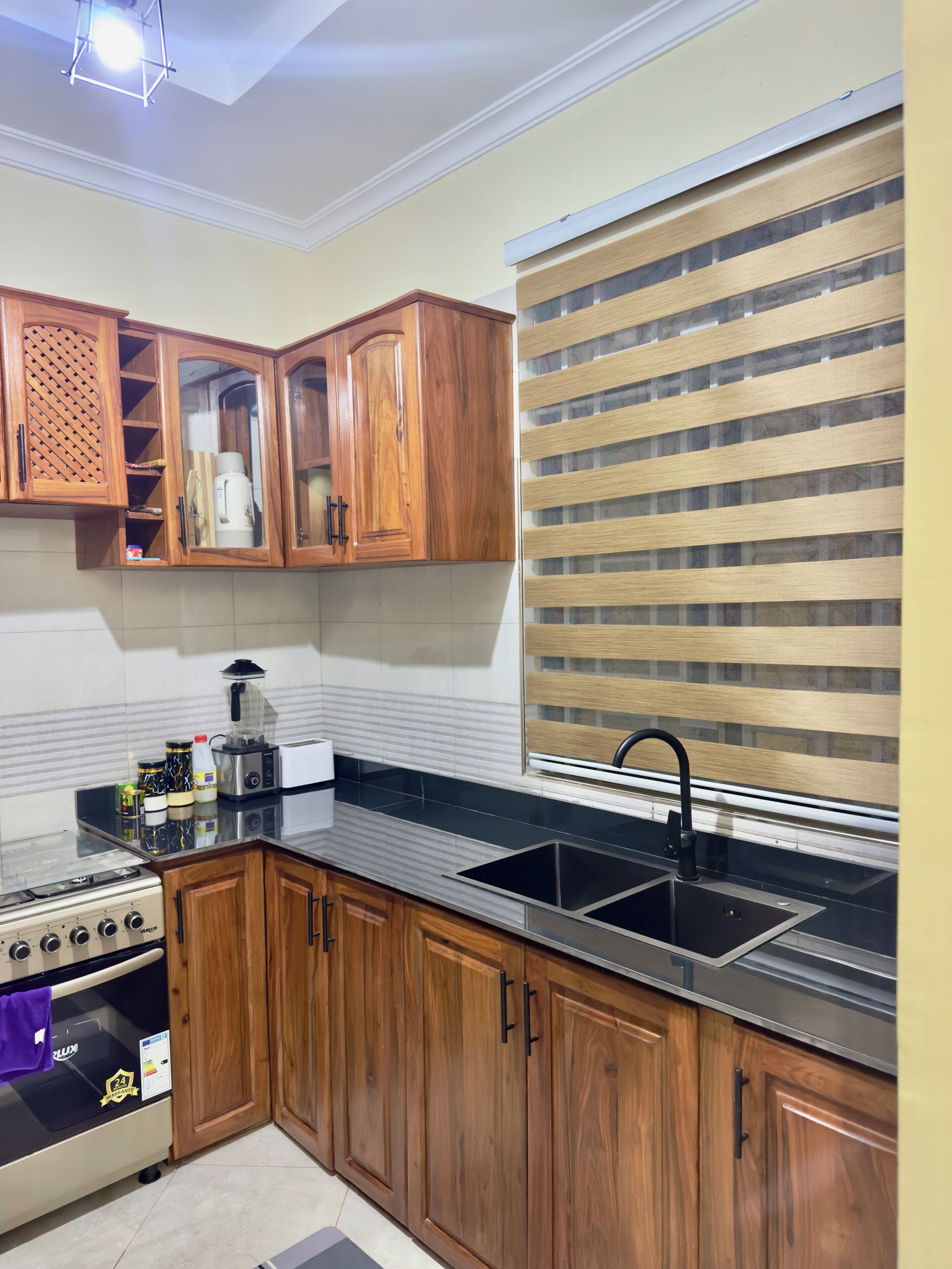 A kitchen with wooden cabinets, a black countertop, a stainless steel sink, and a stove.