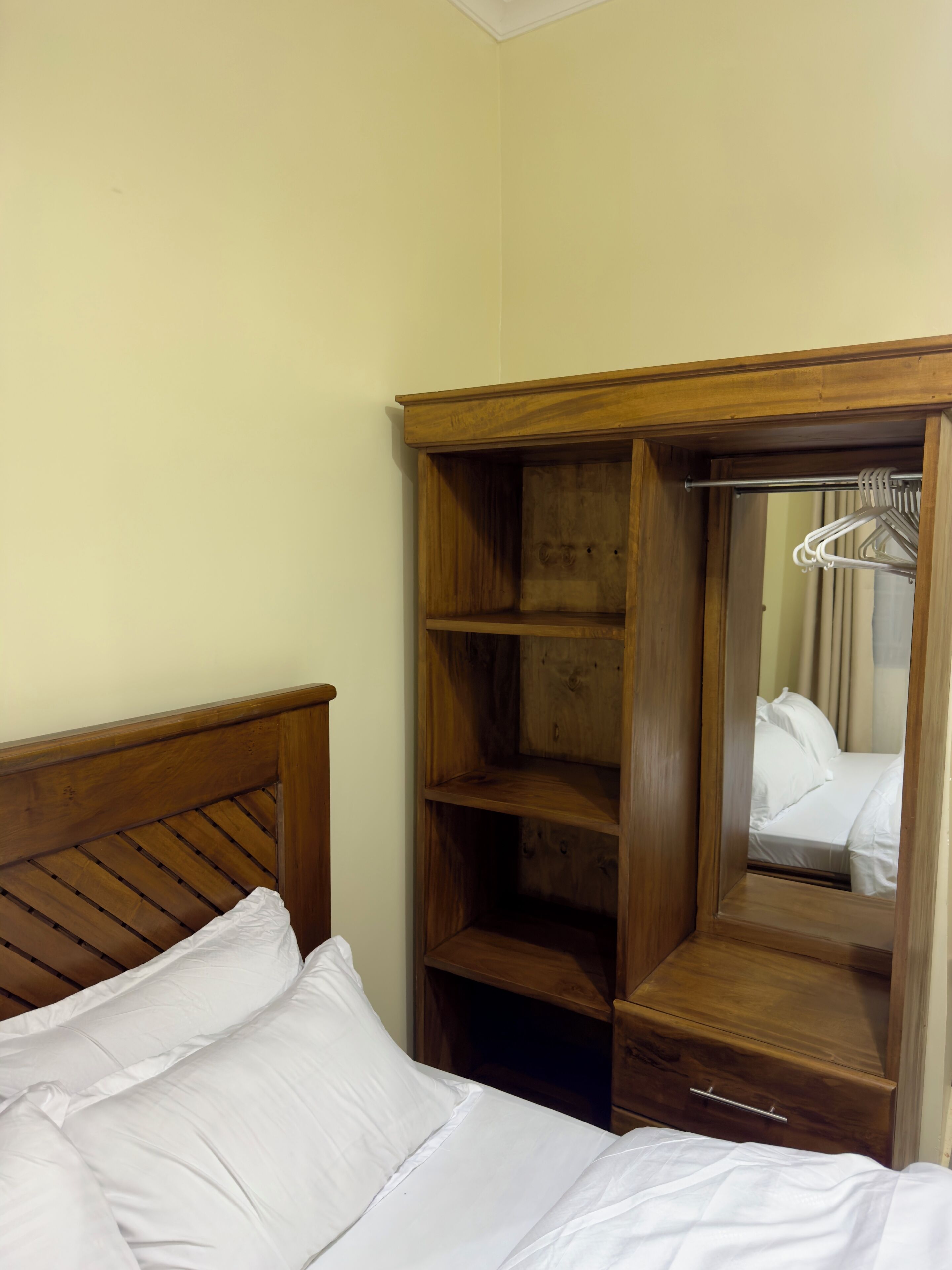Une chambre d’hôtel avec une tête de lit en bois, un grand miroir et une armoire dotée de plusieurs étagères et d’un espace pour suspendre les vêtements.