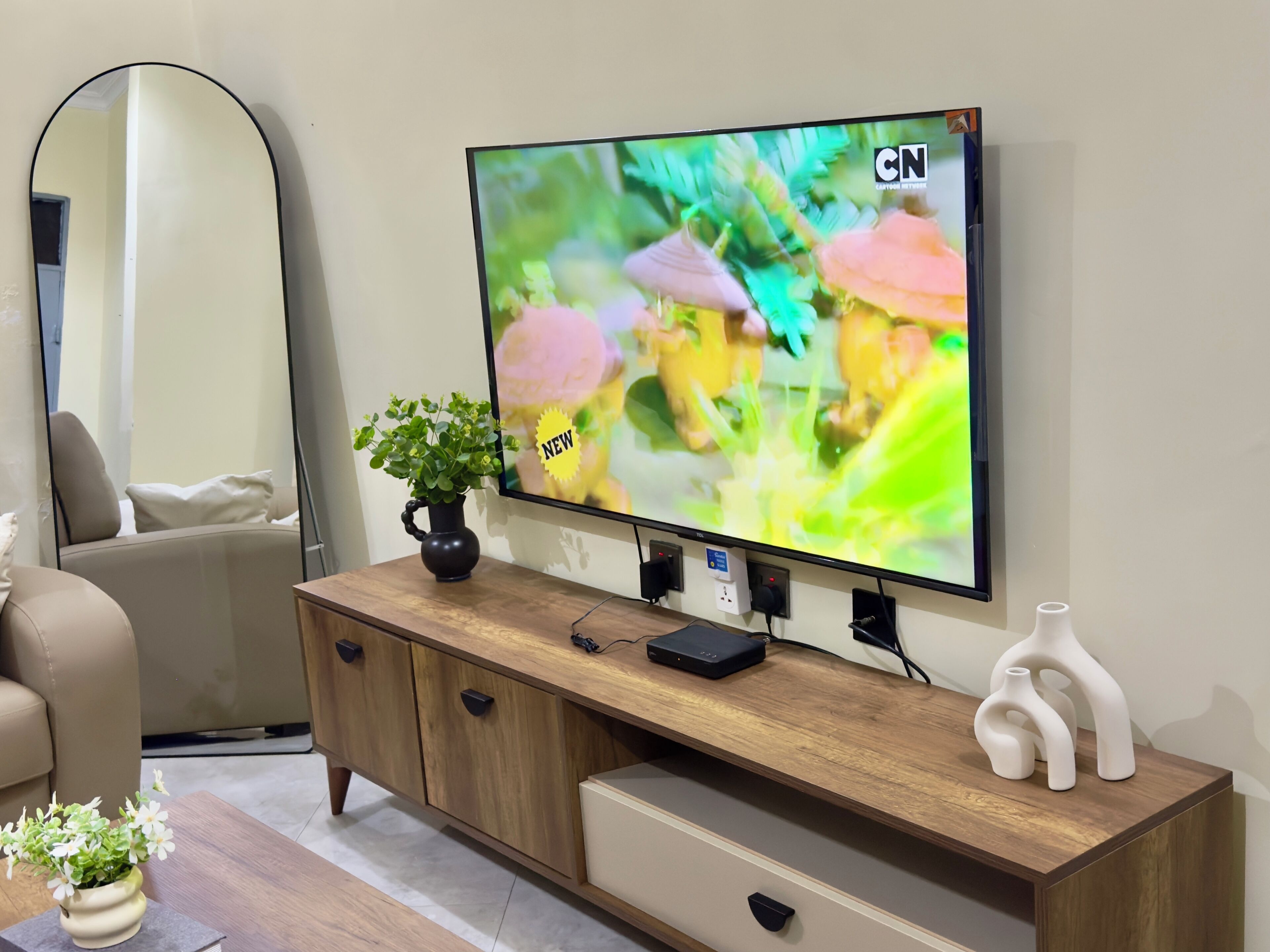 Un téléviseur fixé sur un meuble en bois, avec un vase de fleurs et un objet décoratif posés sur le dessus.