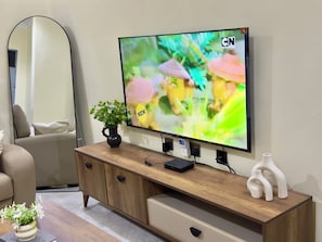 A television mounted on a wooden cabinet with a flower vase and a decorative item on top. - Aiden House Arusha: 2BR Apartment, Free Parking/WiFi, Close to Arusha Centre (Arusha)