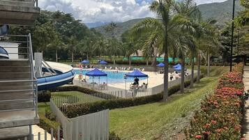Zona de piscina con tobogán acuático, rodeada de palmeras y una valla de madera.