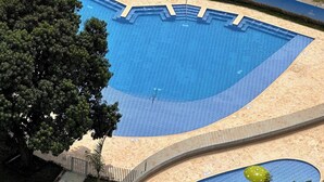 Une piscine au design incurvé, entourée d’une terrasse en bois et d’une clôture en métal.