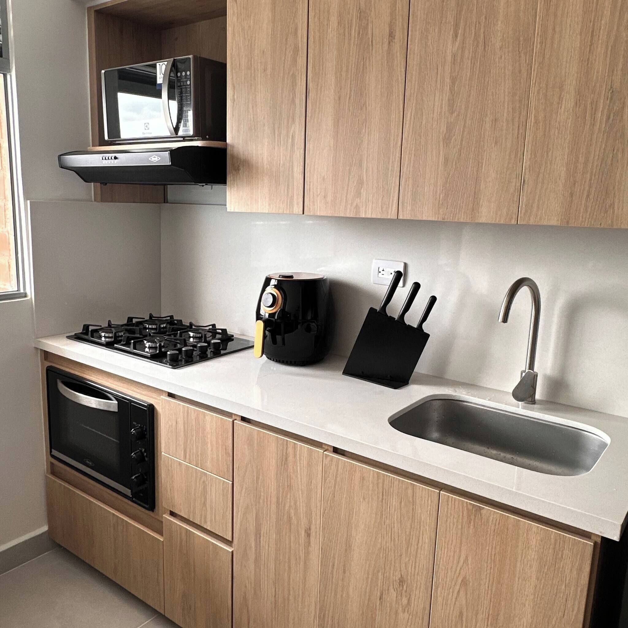Cocina con estufa a gas, horno, pileta y armarios de madera.