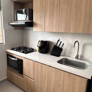 A kitchen with a gas stove, oven, sink, and wooden cabinets. - Epic View 25 • Pablo Tobón Cardiovascular • (Medellín)