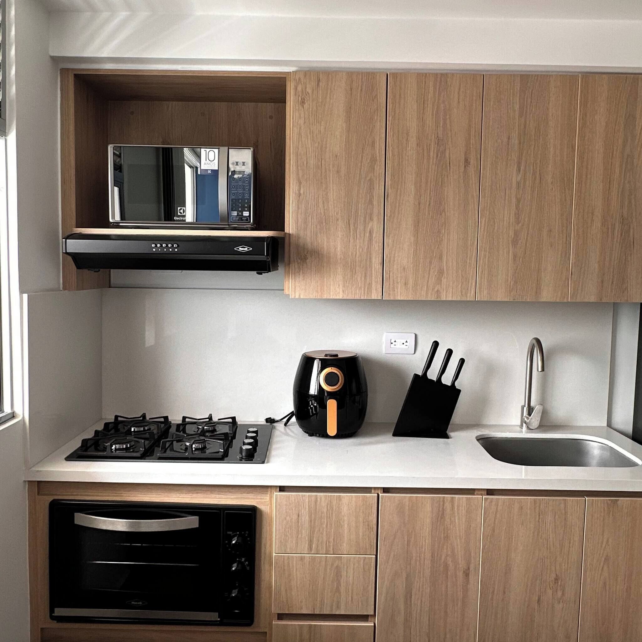 A modern kitchen with wooden cabinets, a built-in microwave, a gas stove, an oven, a coffee maker, and a sink with a faucet.