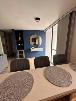 Ein modernes Zimmer mit Esstisch, Stühlen, einem Spiegel und Blick auf eine Küche.