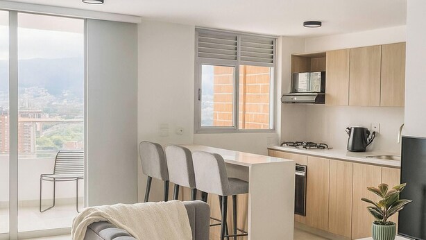 Ein modernes Apartment mit grauem Sofa, Essbereich, Küche und einem Balkon mit Blick auf die Stadt.