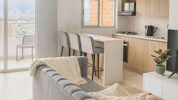 Apartamento moderno con sofá gris, comedor, cocina y balcón con vistas a la ciudad.