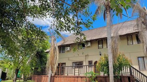 A two-story building with a thatched roof, a wooden fence, and a small pool area. - VM Guesthouse Hazyview Mpumalanga South Africa (Hazyview)