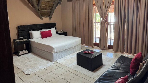 A bedroom with a bed, a nightstand, a black sofa, a small table, and a window with curtains. - VM Guesthouse Hazyview Mpumalanga South Africa (Hazyview)
