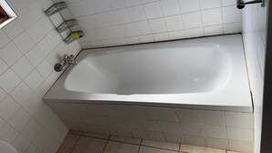 A bathroom with a white bathtub, a shower, and a toilet. There are two shelves with toiletries. - VM Guesthouse Hazyview Mpumalanga South Africa (Hazyview)