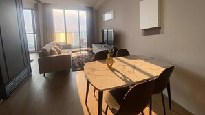En moderne stue med sofa, spisebord med stole, fjernsyn og en balkon med udsigt.