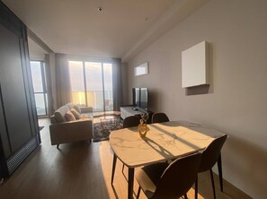 Ein modernes Wohnzimmer mit einer Couch, einem Esstisch mit Stühlen, einem Fernseher und einem Balkon mit Blick.