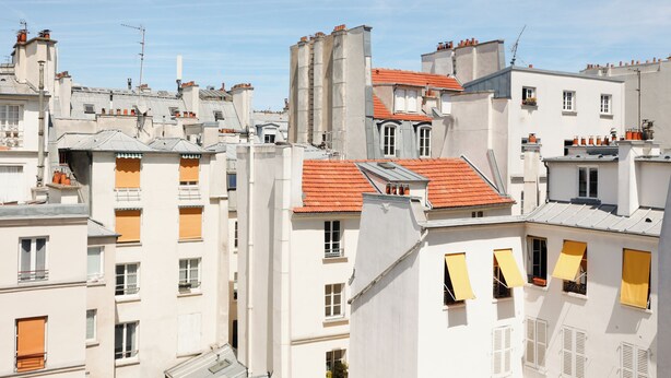 Un edificio de varios pisos con balcones, techo de tejas rojas y fachada blanca.