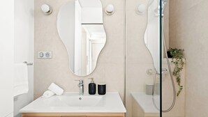 Un baño moderno con un espejo grande, un lavamanos, una ducha y una planta en maceta.
