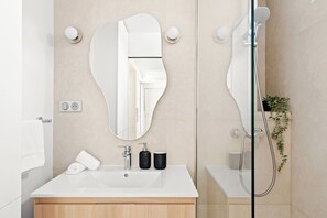 A modern bathroom with a large mirror, a sink, a shower, and a potted plant. - Chic 2BR in the Heart of Paris 2 (Paris)