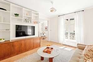 A modern living room with a TV, wooden cabinet, and a dining area with a table and chairs. - Chic 2BR in the Heart of Paris 2 (Paris)