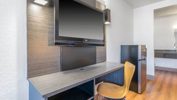 A modern living space with a flat-screen TV mounted on a wall, a wooden chair, and a built-in kitchen area. - 2 Full Beds|Renovated,Mini Fridge (Hayward)