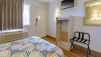 A room with a bed, a window with curtains, a TV mounted on the wall, a heater, and a chair.