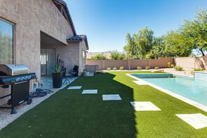 A backyard with artificial grass, a swimming pool, a barbecue grill, and a patio area with chairs and a table. - 5 Mi to Estrella Mtn Park! Home w/ Outdoor Oasis (Goodyear)