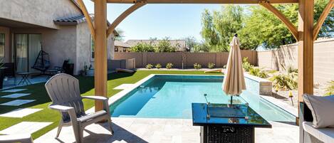 A covered outdoor swimming pool area with a lounge chair, a table with an umbrella, and a patio table.