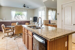 A modern kitchen with granite countertops, a dishwasher, and a dining area with a sofa and chairs. - 5 Mi to Estrella Mtn Park! Home w/ Outdoor Oasis (Goodyear)