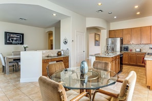 A modern kitchen with a central island, wooden cabinets, and a dining area with a glass table and chairs. - 5 Mi to Estrella Mtn Park! Home w/ Outdoor Oasis (Goodyear)
