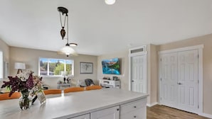 A kitchen with a large island, white cabinetry, and a view of a cityscape through the window. - The Nest House (Burlington)