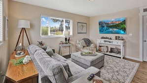 A living room with a sofa, ottoman, and a television mounted on the wall. - The Nest House (Burlington)