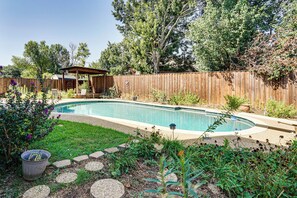 Ein Garten mit Schwimmbecken, einer Holzterrasse und einem eingezäunten Bereich.