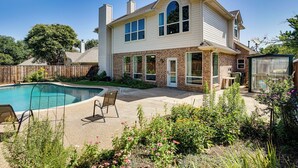 Una casa a due piani con piscina nel cortile, un patio con sedie e un giardino con diverse piante.