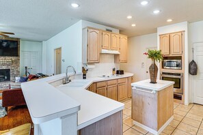 A modern kitchen with a central island, wooden cabinets, a built-in microwave, and a stone fireplace. - Arlington Home w/ Pool: Just Over 1 Mi to Stadium (Arlington)