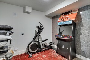 A room with a stationary bike, a small sink, and a wall-mounted arcade machine. - Quiet Tooele Retreat w/ Games + Fireplace (Tooele)