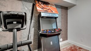 A room with a gaming arcade machine and a stationary exercise bike. - Quiet Tooele Retreat w/ Games + Fireplace (Tooele)