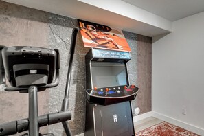 A room with a gaming arcade machine and a stationary exercise bike. - Quiet Tooele Retreat w/ Games + Fireplace (Tooele)