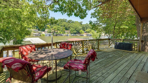 Une terrasse en bois avec une table ronde et des chaises, d’où l’on a vue sur une étendue d’eau, avec des bateaux et des bâtiments en arrière-plan.