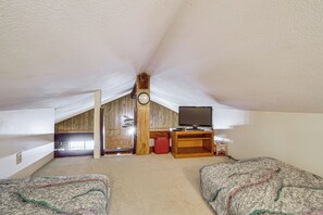 Ein Dachzimmer mit Holzbalkendecke, einer Uhr, einem Fernseher auf einem Holzschrank und zwei Betten mit gemusterten Betttextilien.