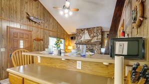 Une cuisine avec des murs en bois, un mur d’accent en pierre, un ventilateur de plafond, un téléviseur d’époque et un bloc à couteaux.