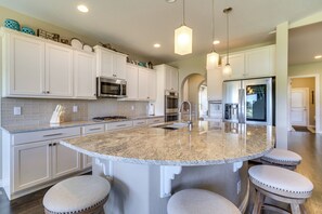 Una cocina con gabinetes blancos, encimeras de granito, electrodomésticos de acero inoxidable y taburetes de bar.